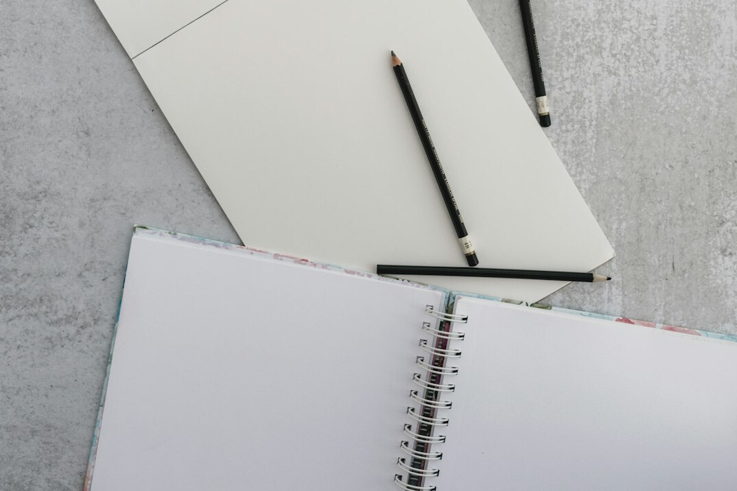 Person writing notes in a notebook next to an open laptop